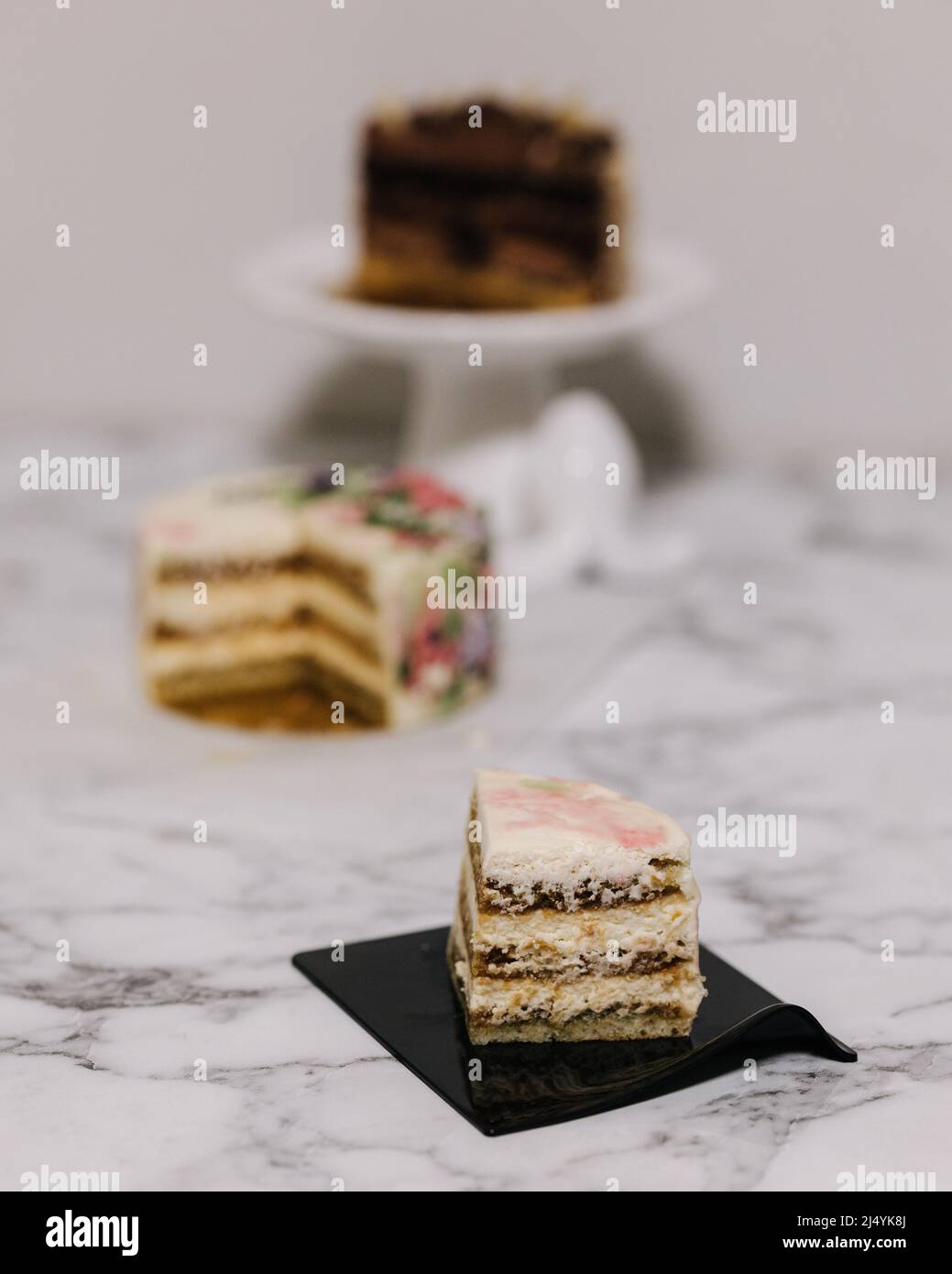 Scheibe Tiramisu-Bento-Kuchen. Präsentation des Kuchens im Abschnitt. Süßes Dessert für eine Person. Kleiner Geburtstagskuchen. Hintergrund von anderen Bento-Kuchen Stockfoto