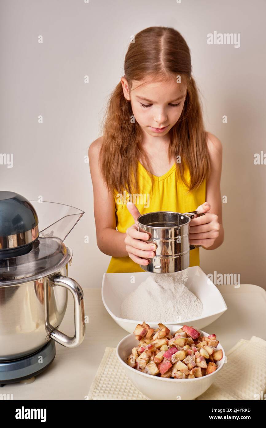 Ein Teenager-Mädchen kocht einen hausgemachten Kuchen, einen Kuchen mit Äpfeln in der Küche. Mischt die Zutaten für den Kuchen in einem elektrischen Mixer. Nahaufnahme. Stockfoto