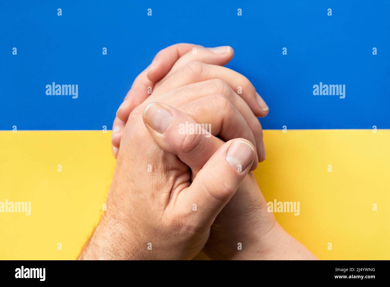 Klatschende Hände, Nahaufnahme von kaukasischen männlichen und weiblichen Händen. Flach liegend, Draufsicht auf blaugelbem Papierhintergrund, Ukraine-Flaggenfarben. Stockfoto
