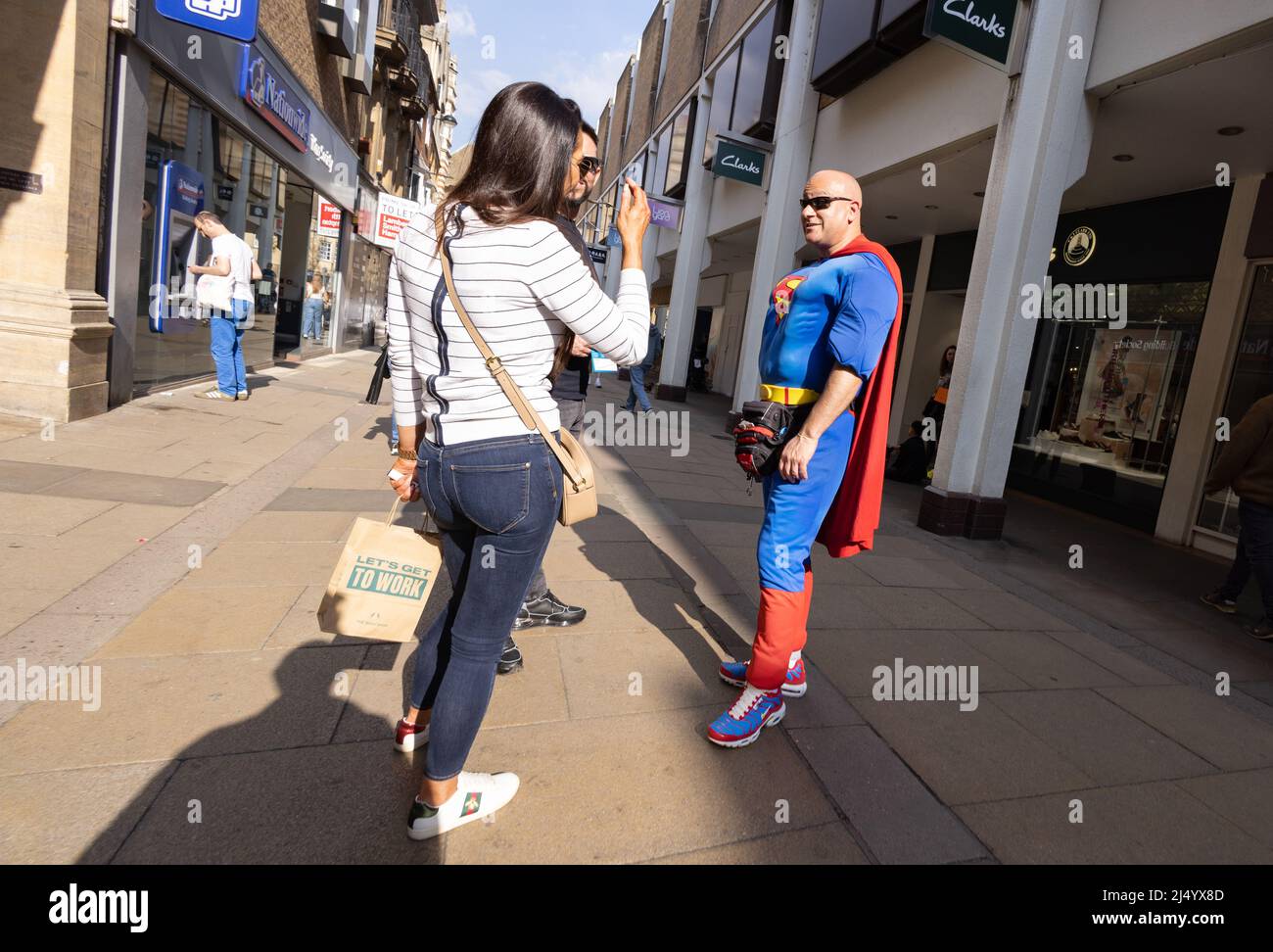Mann im Superman-Kostüm im Gespräch mit Menschen, Cambridge, Großbritannien; ehrliche Straßenfotografie, Großbritannien. Exzentrisches englisch. Stockfoto