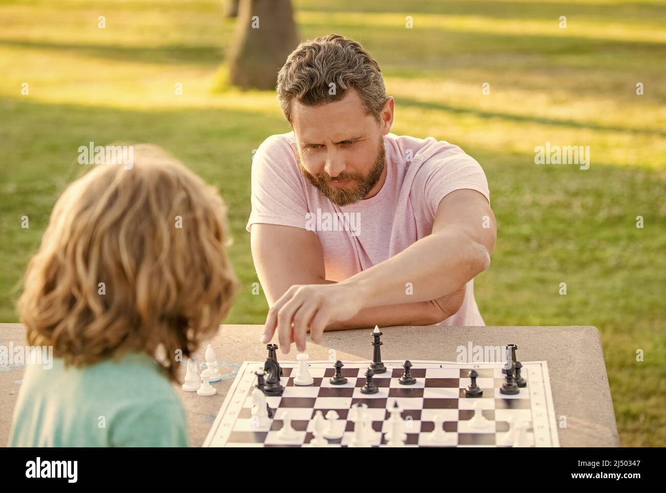 Glückliche Familie von Vater und Sohn Kind spielen Schach auf dem Tisch im Park im Freien, analytisches Denken Stockfoto