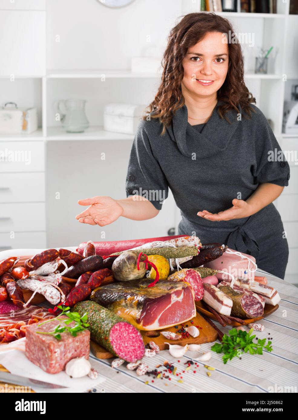 Frau kostet neben dem Tisch, auf dem Würstchen und geräuchertes Fleisch Stockfoto