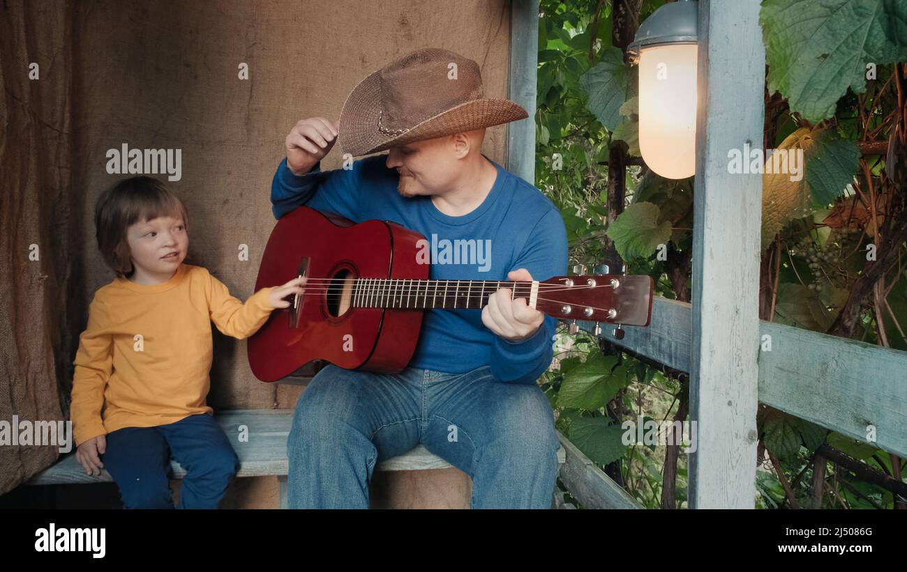 Papa Cowboy spielt für sein kleines Kind eine akustische Gitarre. Altes Retro-Dekor Stockfoto