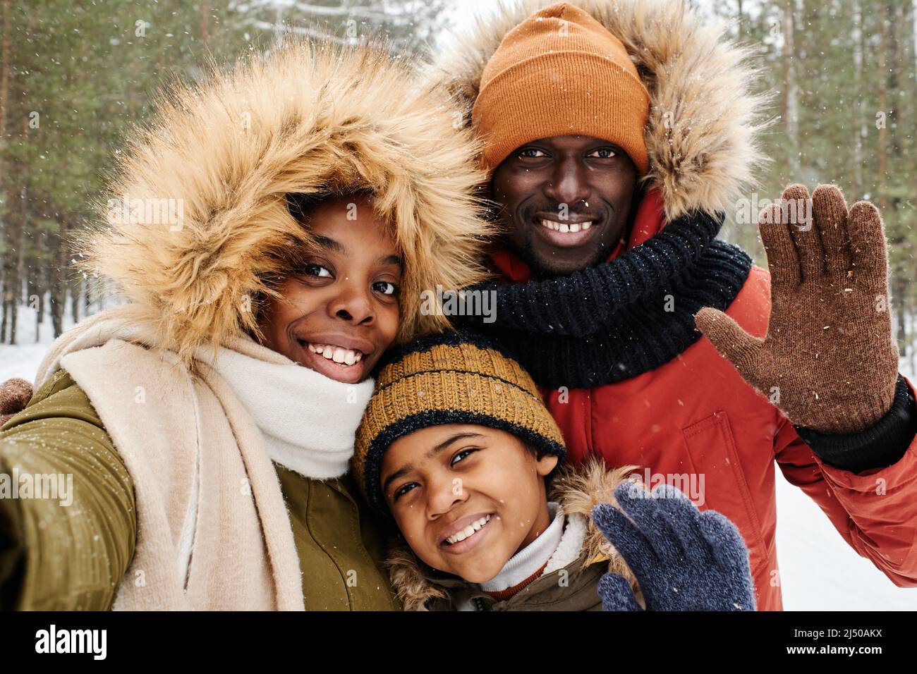 Eine afroamerikanische dreiköpfige Familie in Winterkleidung begrüßt Sie, während Sie an einem frostigen Wintertag in Ruhe die Kamera im Park oder Wald betrachten Stockfoto