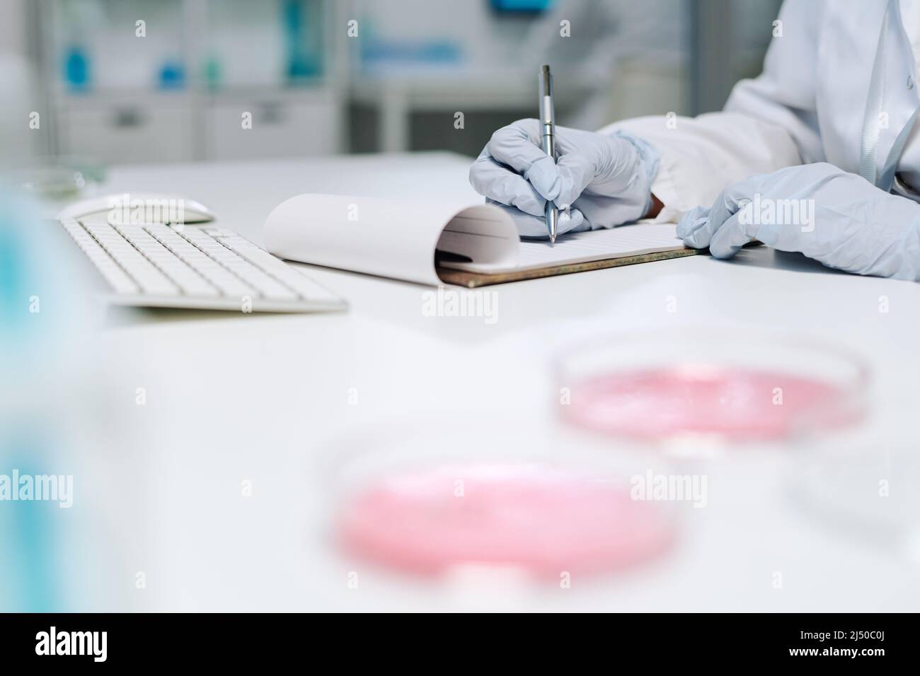 Handschuhen eines modernen Klinikers oder Biochemikers, der die Ergebnisse wissenschaftlicher Experimente am Arbeitsplatz aufschreibt Stockfoto