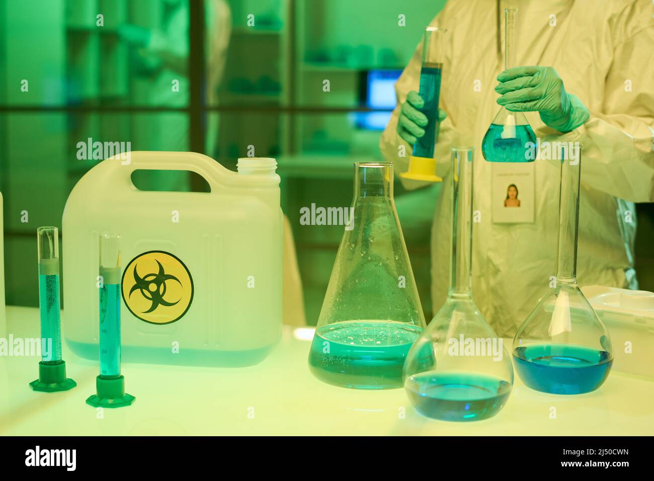 Moderner Arzt in Overalls und Handschuhen, die zwei Reagenzgläser mit blauer, flüssiger toxischer Substanz halten, während er am Arbeitsplatz im Labor steht Stockfoto