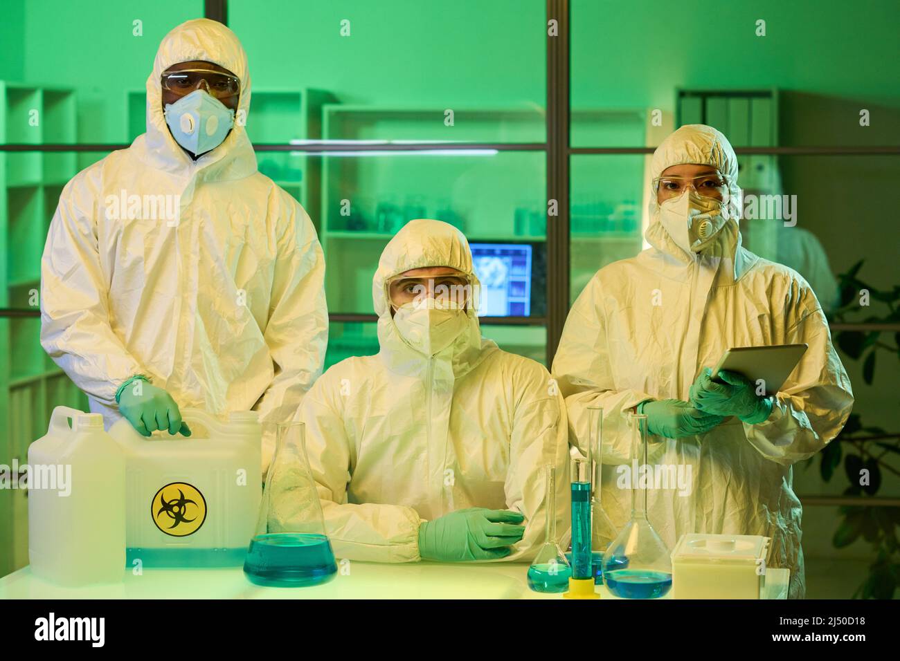 Gruppe junger interkultureller Wissenschaftler oder Labormitarbeiter in Schutzkleidung, Handschuhen, Brillen und Atemschutzmasken, die die Kamera betrachten Stockfoto