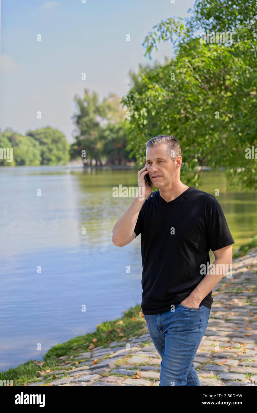 Reifer Geschäftsmann, der an einem See mit dem Handy telefoniert Stockfoto