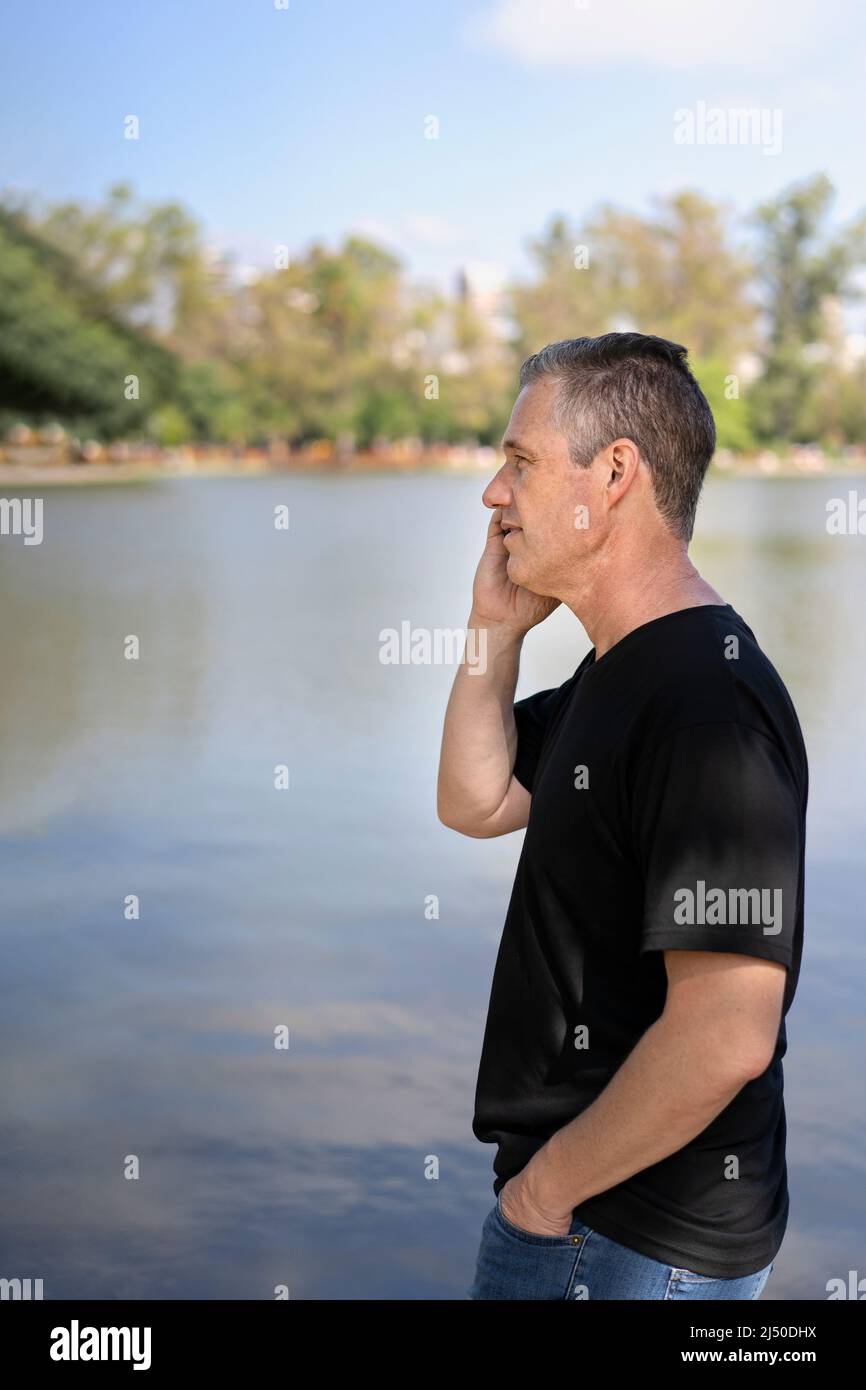 Reifer Geschäftsmann, der an einem See mit dem Handy telefoniert Stockfoto