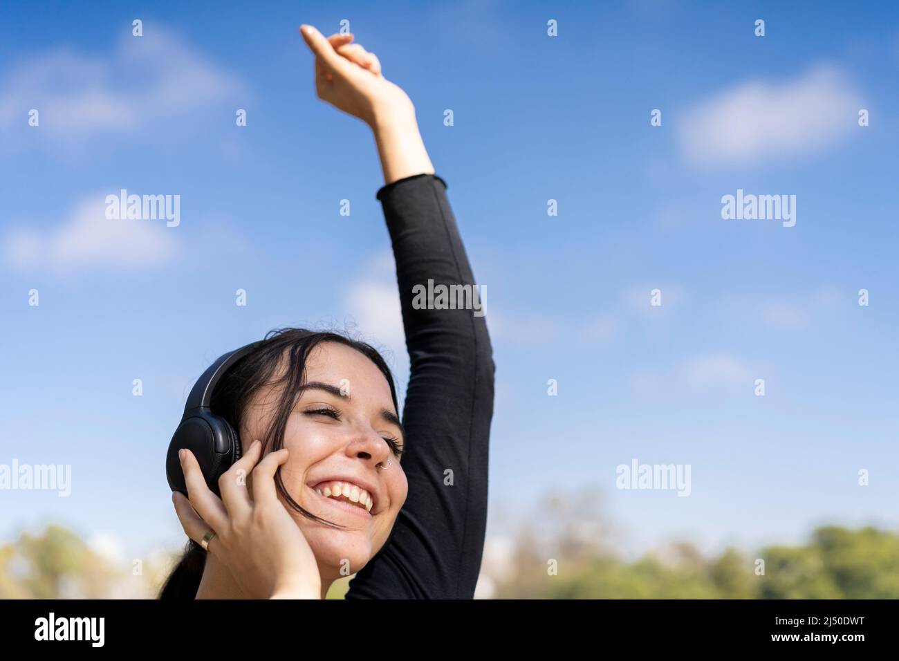Junge Frau hört Musik im Freien mit bluetooth-Kopfhörern. Ausdruck von Glück, gewinnende Haltung. Speicherplatz kopieren Stockfoto