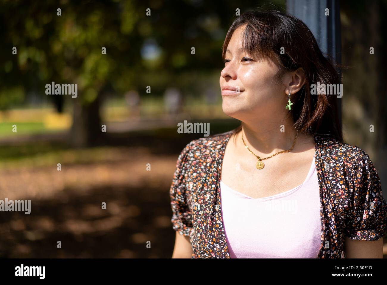 Porträt einer jungen Lateinerin in einem Park, die sich auf einen Laternenpfosten stützt und die Sonnenstrahlen auf ihrer Haut genießt Stockfoto