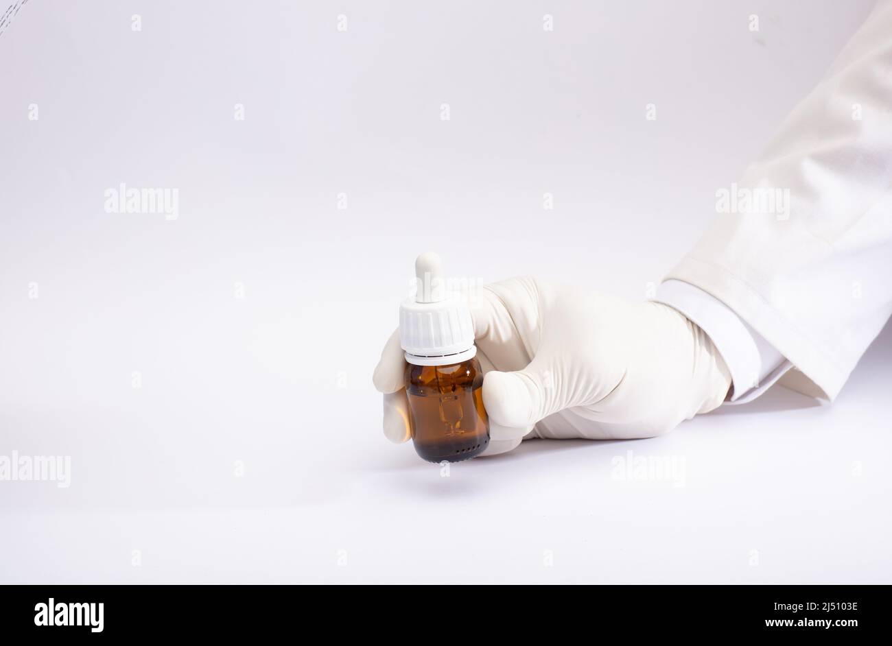Marihuanaöl in Tropfenspender-Flasche in Handschuhen, weißer Hintergrund Stockfoto