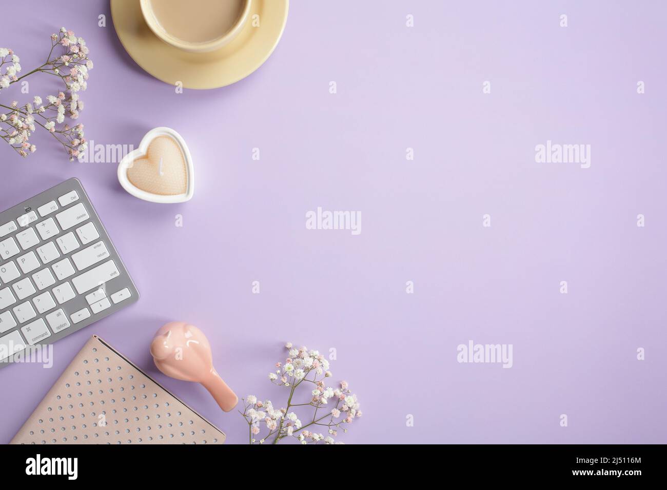 Flach liegend, Draufsicht niedlichen Bürotisch Schreibtisch. Femininer Arbeitsplatz mit Tastatur, Kaffeetasse, Notizbuch, herzförmiger Kerze, Vogel, Blüten auf pastellviolett Stockfoto