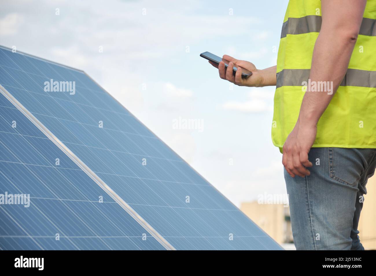 Nicht erkennbare Person, die ein Telefon zur Steuerung einer Photovoltaikanlage verwendet. Stockfoto