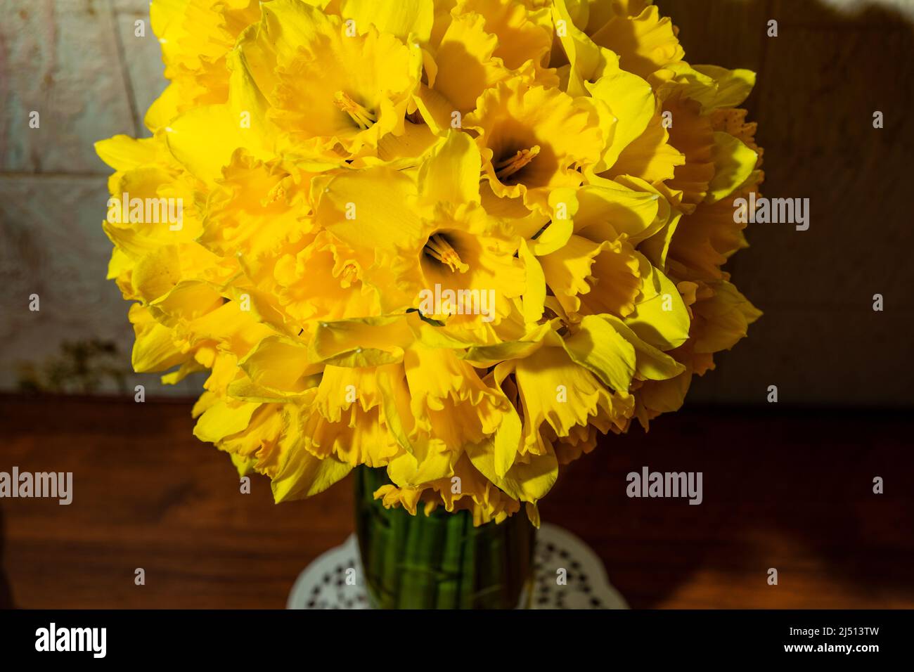 Ein großer Strauß gelber Narzissen in einer Vase auf einem Holztisch, Stockfoto