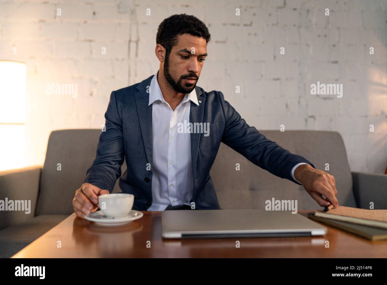 Beschäftigter junger Geschäftsmann, der Kaffee trinken und seine Arbeit erledigen kann. Stockfoto