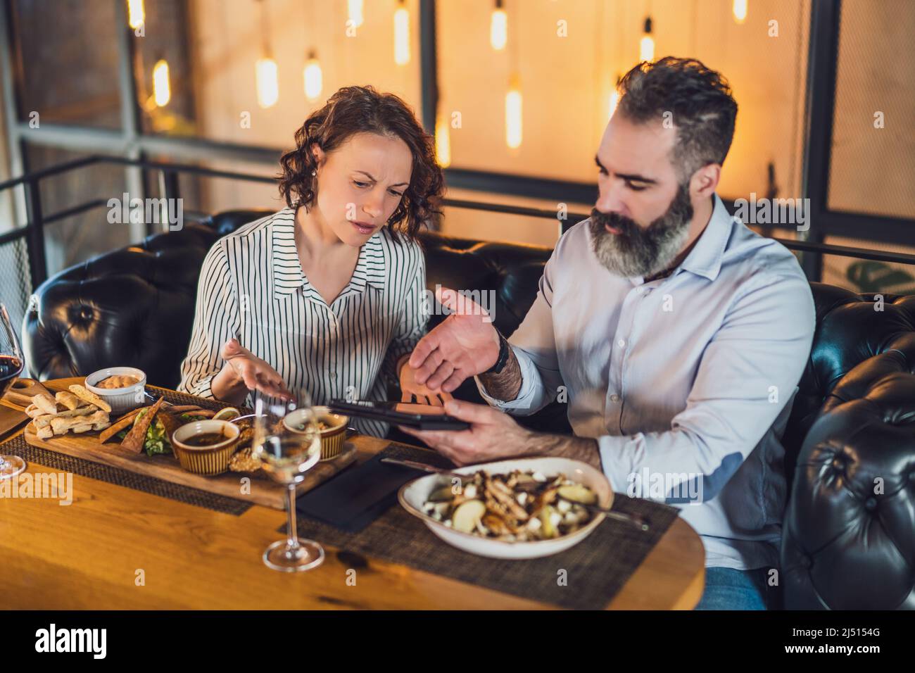 Das Paar sitzt im Restaurant. Sie essen zu Mittag, nutzen digitale Tablets und streiten sich. Stockfoto
