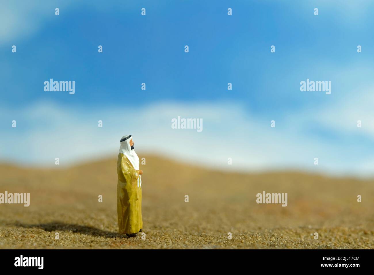 Miniatur Menschen Spielzeug Figur Fotografie. Ein Sultan in gelbem Bihst, Königskleie, steht in der Wüste in hellem Himmel. Bildfoto Stockfoto