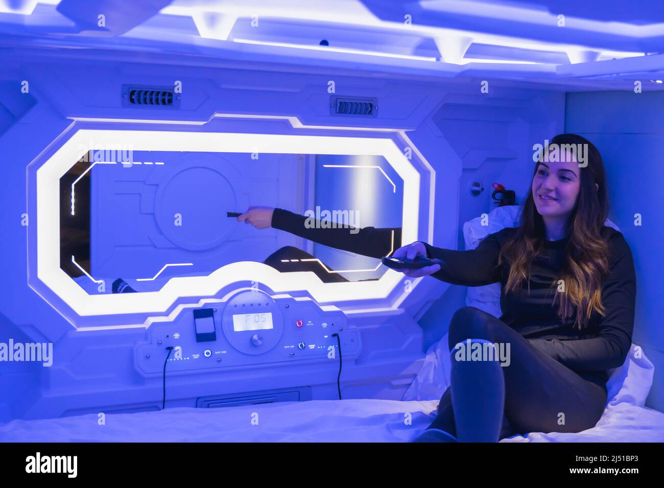 Frau im Schlafzimmer der Kapsel, die den fernseher anmacht Stockfoto