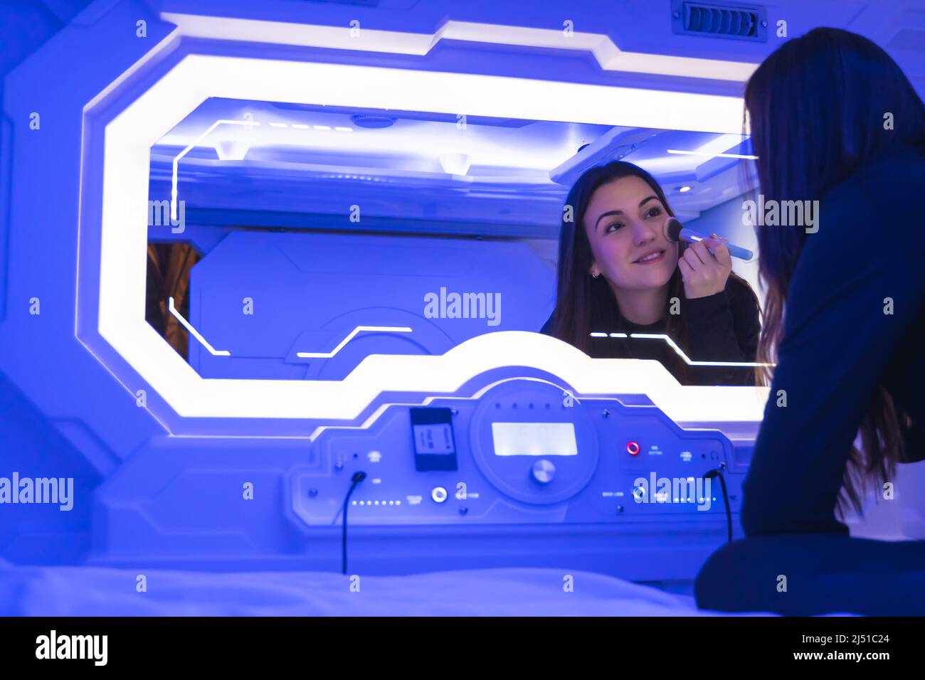 Frau, die sich im Spiegel der Schlafkapsel schminkt. Stockfoto