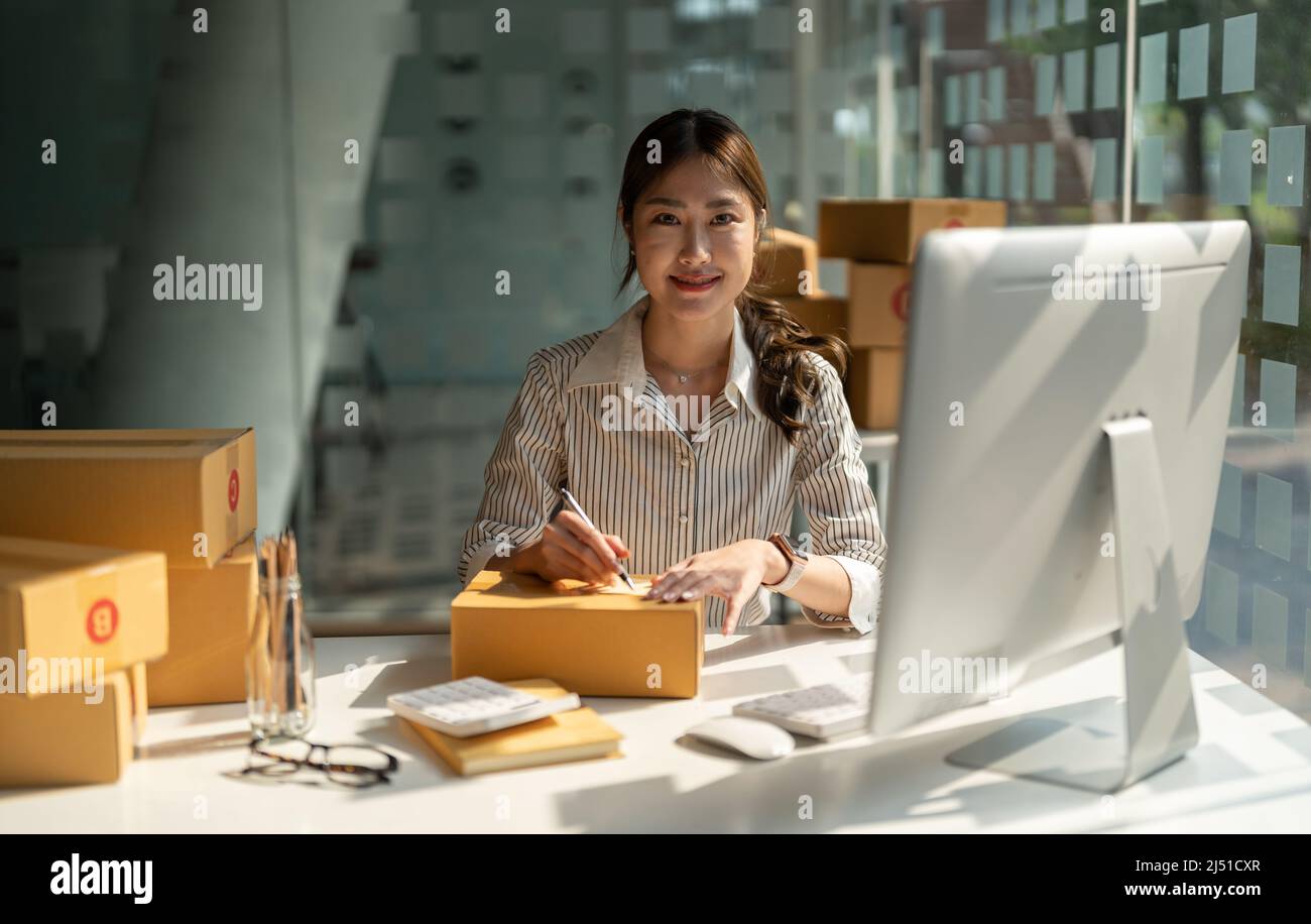 Junger asiatischer Kleinunternehmen, der im Heimbüro arbeitet und die Bestellungen zur Kenntnis nimmt. Online-Marketing Verpackung Lieferung, Startup KMU Unternehmer Stockfoto