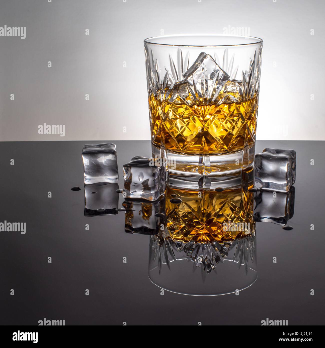 Glas Whisky mit Eis, hinterleuchtet auf einem reflektierenden schwarzen Vordergrund in einem Glasbecher. Stockfoto