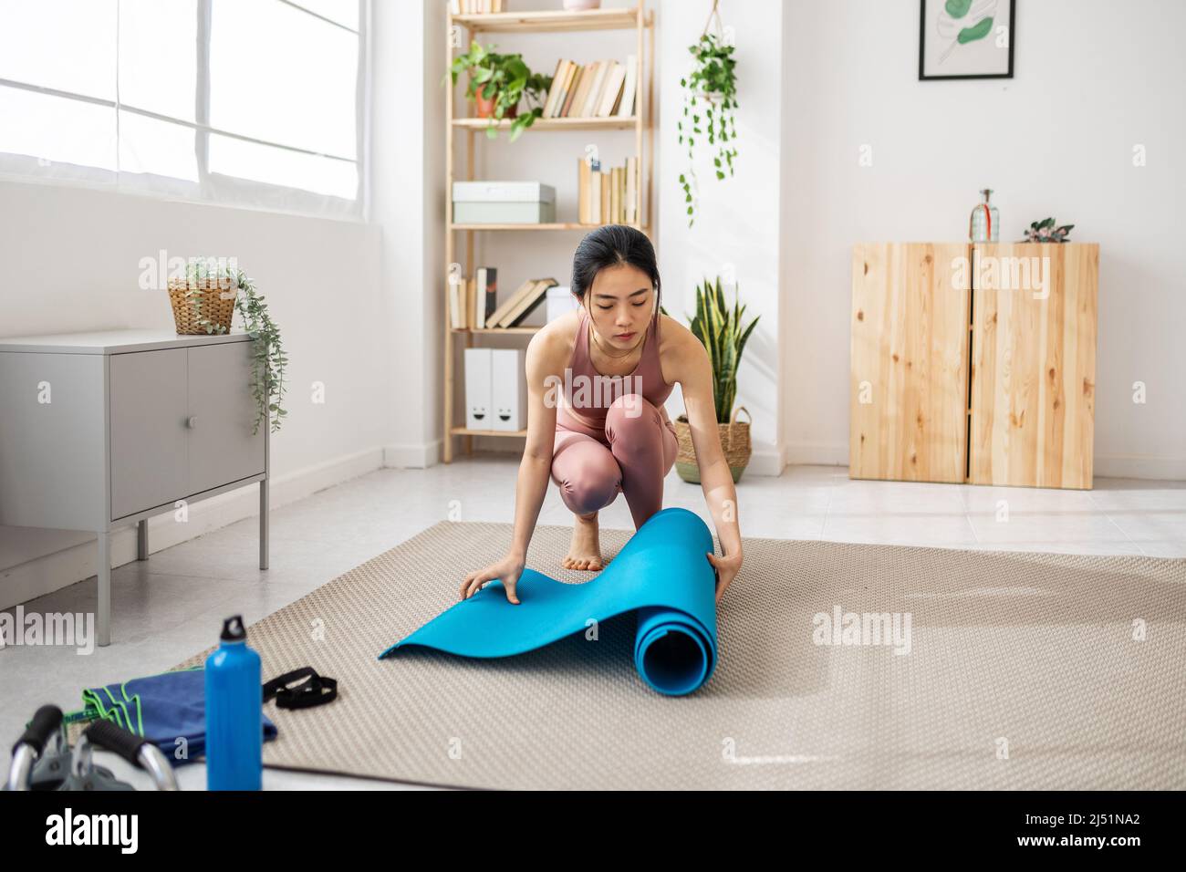 Frau, die eine Yogamatte ausrollt, während sie sich auf die Fitnessübungen zu Hause vorbereitet Stockfoto