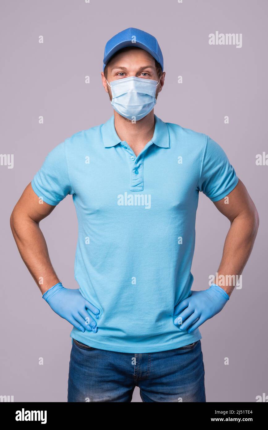 Junger Mann in blauer Uniform mit einer Schutzmaske und isolierten Handschuhen auf grauem Hintergrund Stockfoto