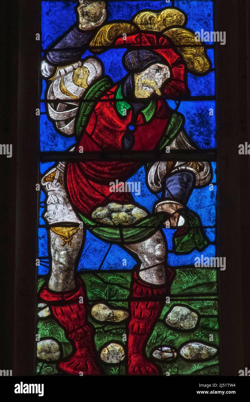 Ein Henker in einem Kostüm aus dem 16.. Jahrhundert schleudert Steine auf den ersten christlichen Märtyrer, den heiligen Stephanus, in einem lebendigen Detail von Glasmalereien Anfang 1500s im Église Saint-Rémi in Ceffonds, in der Champagne-Region im Nordosten Frankreichs. Die Farben sind typisch für Renaissance-Glas, das in den Werkstätten von Troyes, der historischen Hauptstadt der Region, hergestellt wurde. Stockfoto