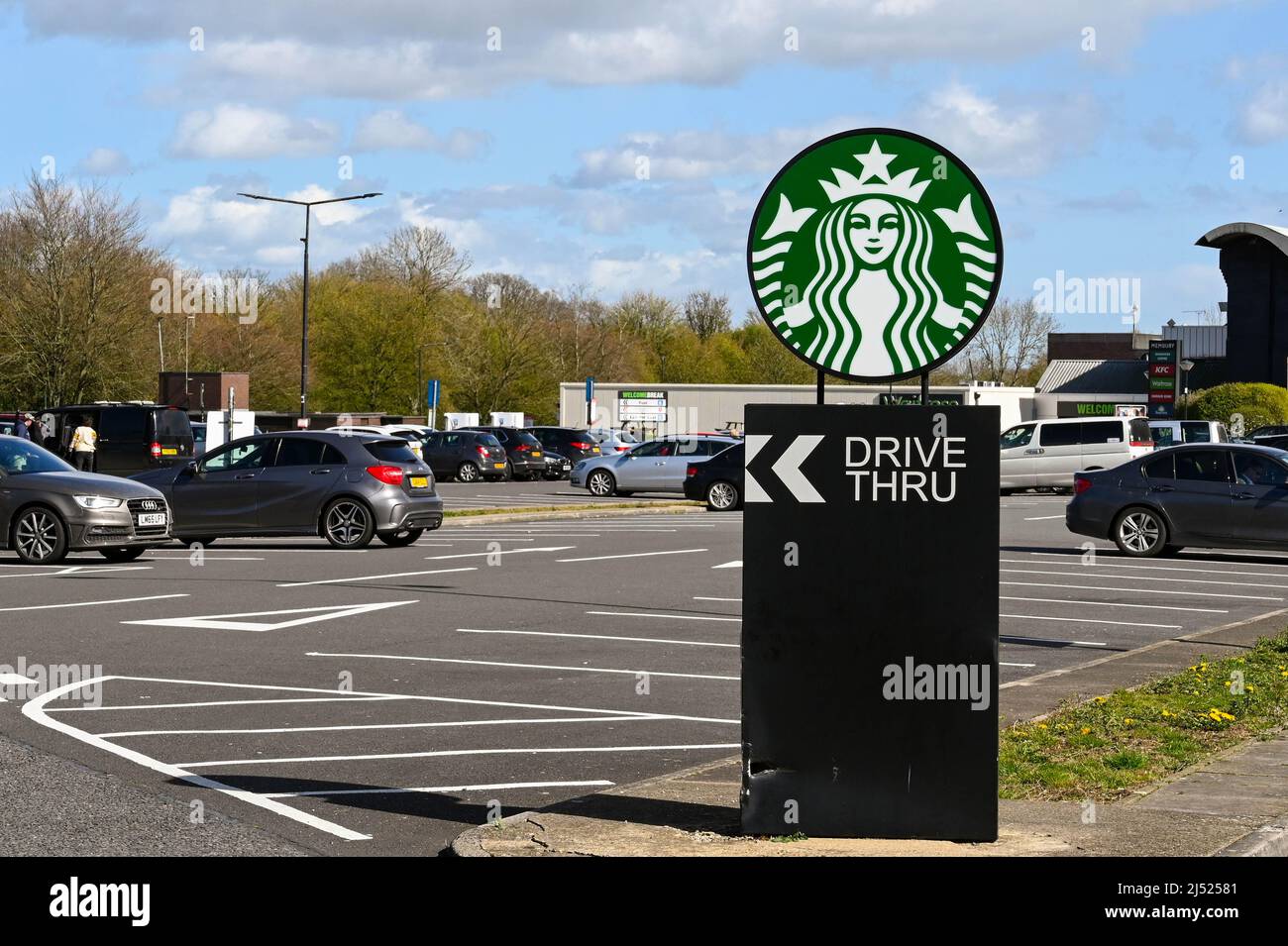 Swindon, England - April 2022: Schild auf dem Parkplatz einer Tankstelle auf der Autobahn M4, das eine Drive-Thru-Filiale von Starbucks anwirbt Stockfoto