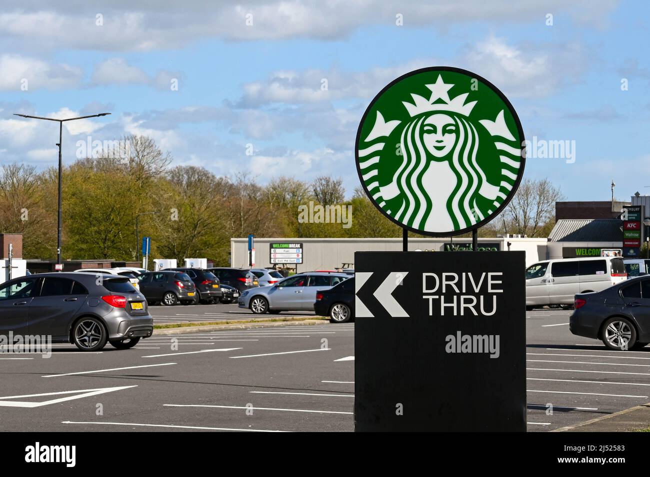 Swindon, England - April 2022: Schild auf dem Parkplatz einer Tankstelle auf der Autobahn M4, das eine Drive-Thru-Filiale von Starbucks anwirbt Stockfoto