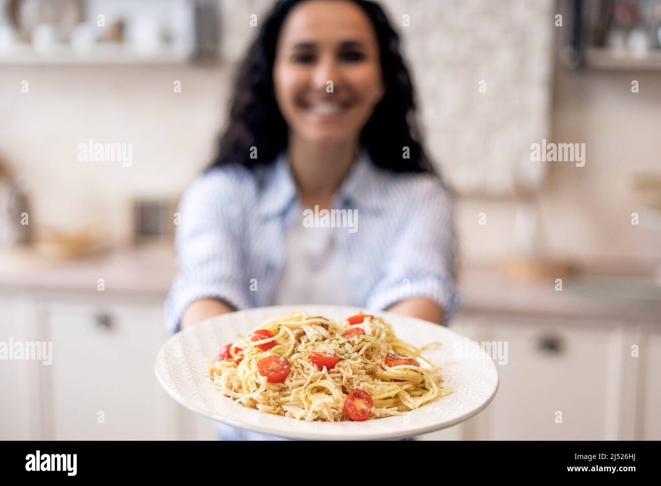 Frau zeigt hausgemachte Pasta im Gericht, dehnt Mahlzeit zur Kamera und lächelt, konzentrieren sich auf Teller mit Spaghetti Stockfoto