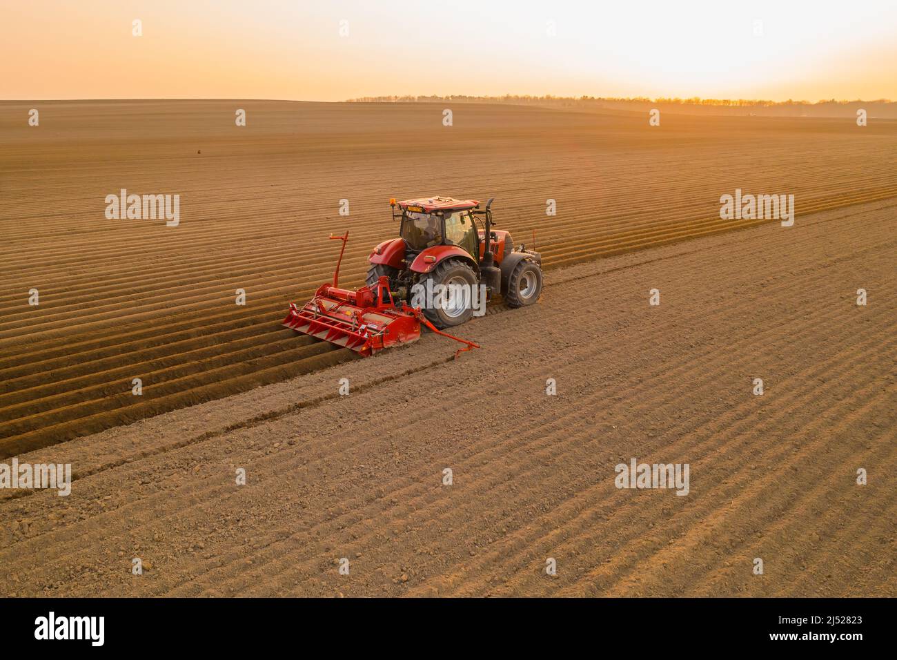 PRAG , TSCHECHISCHE REPUBLIK - MÄRZ 18 2022: Landwirtschaftliche Maschine bereitet lange Betten für die Pflanzung von Kartoffeln auf Kulturfeld. Der rote Traktor zieht den Pflug hinter die Luftaufnahme Stockfoto