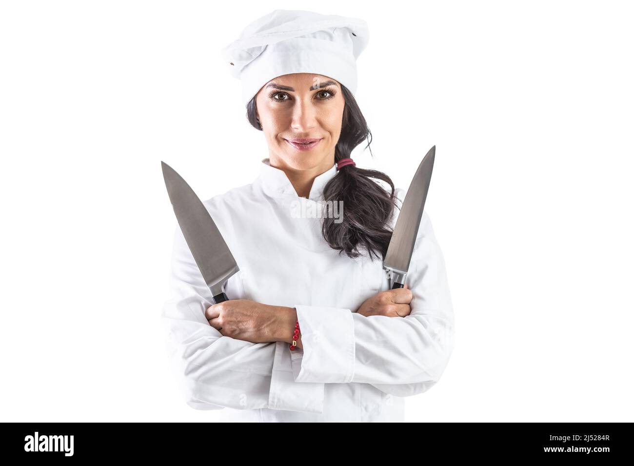 Weibliche Köchin steht mit gekreuzten Armen und hält zwei scharfe Messer - isoliert auf weiß. Stockfoto