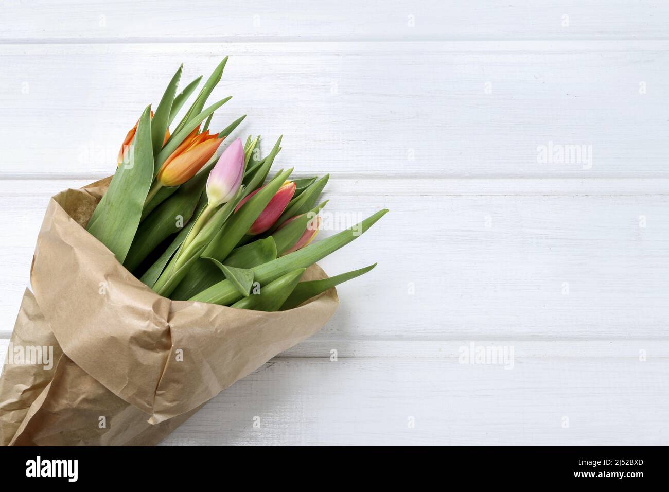 Ein Bouquet aus bunten Tulpen in einer Papierverpackung. Weißer Holzhintergrund, Kopierraum. Stockfoto