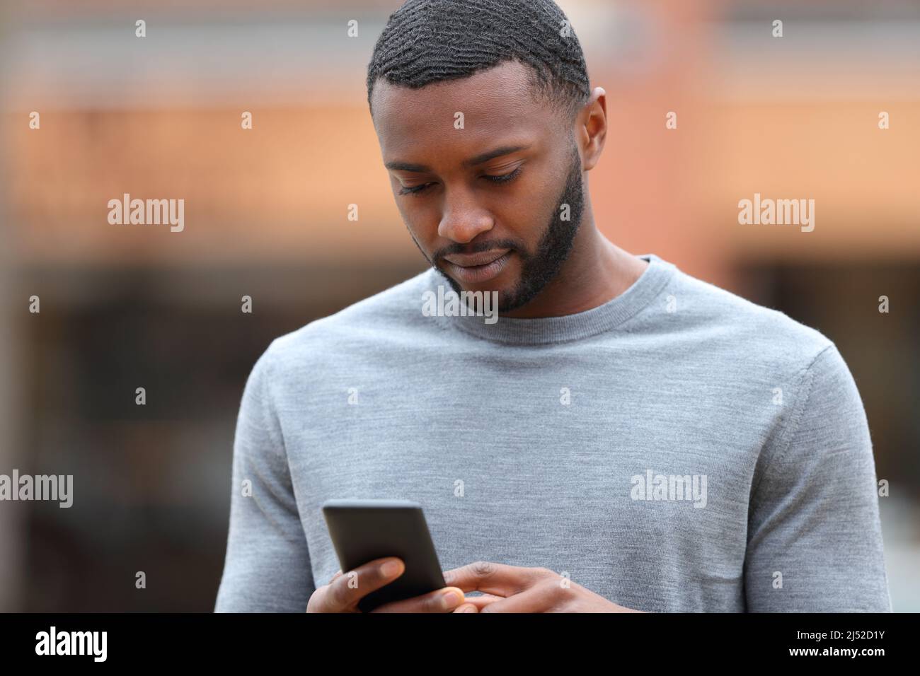 Ernsthafter Mann mit schwarzer Haut nutzt Smartphone auf der Straße Stockfoto