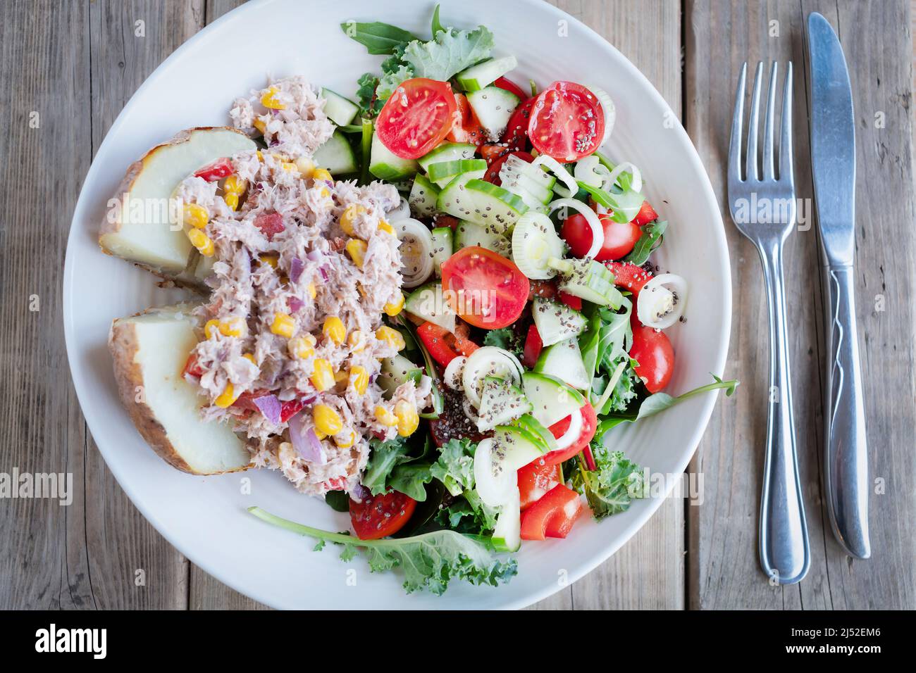 Tun, Mais und Mayonnaise auf einer halben Jackenkartoffel mit einem Salat aus gemischtem Gemüse, Tomaten, Gurken und Zwiebeln. Eine mediterrane Diät Grundnahrungsmittel Stockfoto
