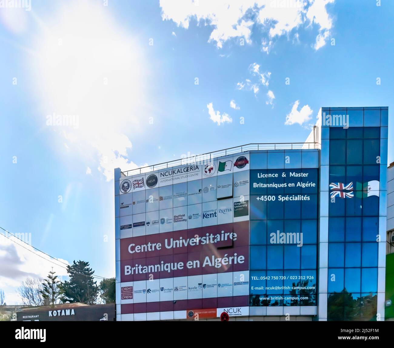 NCUK Algeria International Study Centre Gebäudefassade mit Namensschildplatten, algerischen und britischen Flaggen. Blauer wolkig Himmel und direktes Sonnenlicht. Stockfoto