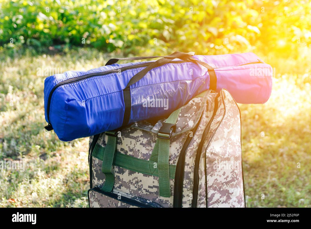 Unschärfe-Militärrucksack und blaues Zelt oder Schlafsack. Army Tasche auf grünem Gras Hintergrund in der Nähe von Baum. Militärrucksack mit Tarnung. Touristen Stockfoto