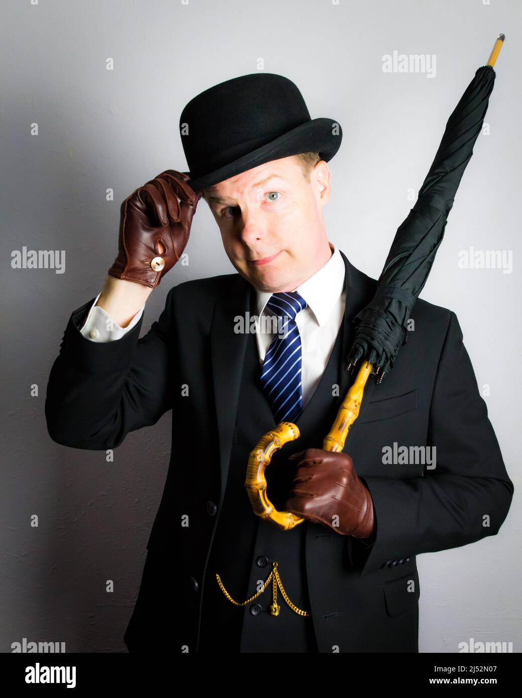 Porträt eines britischen Geschäftsmannes in Dark Suit Holding Regenschirm und höflich doffing Bowler Hut. Vintage Style des eleganten englischen Gentleman. Stockfoto