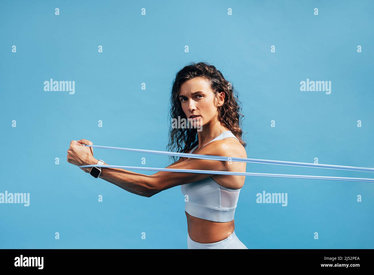 Portrait einer Fitness-Frau, die mit einem Widerstandsband auf blauem Hintergrund Krafttraining macht Stockfoto