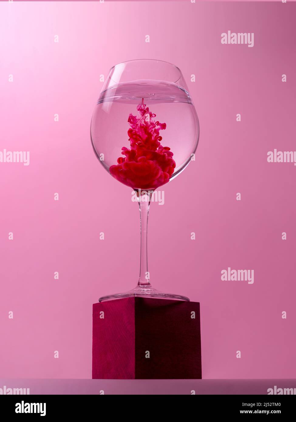 Weinglas auf einem Würfel mit rotem Farbstoff, der sich in Wasser auflöst Stockfoto