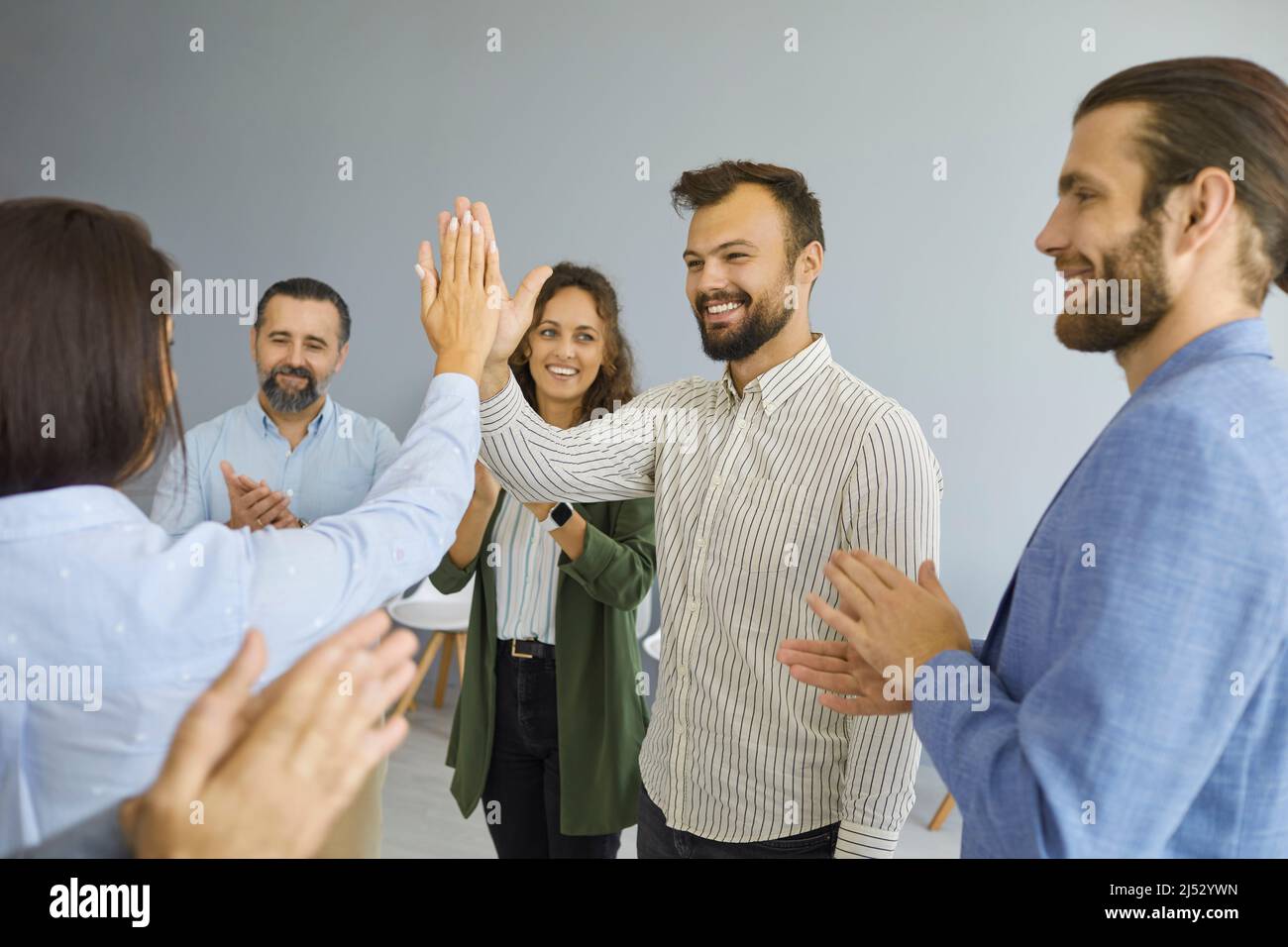 Frau gibt ihrem glücklichen, erfolgreichen männlichen Kollegen fünf zum Applaus anderer Geschäftsleute. Stockfoto