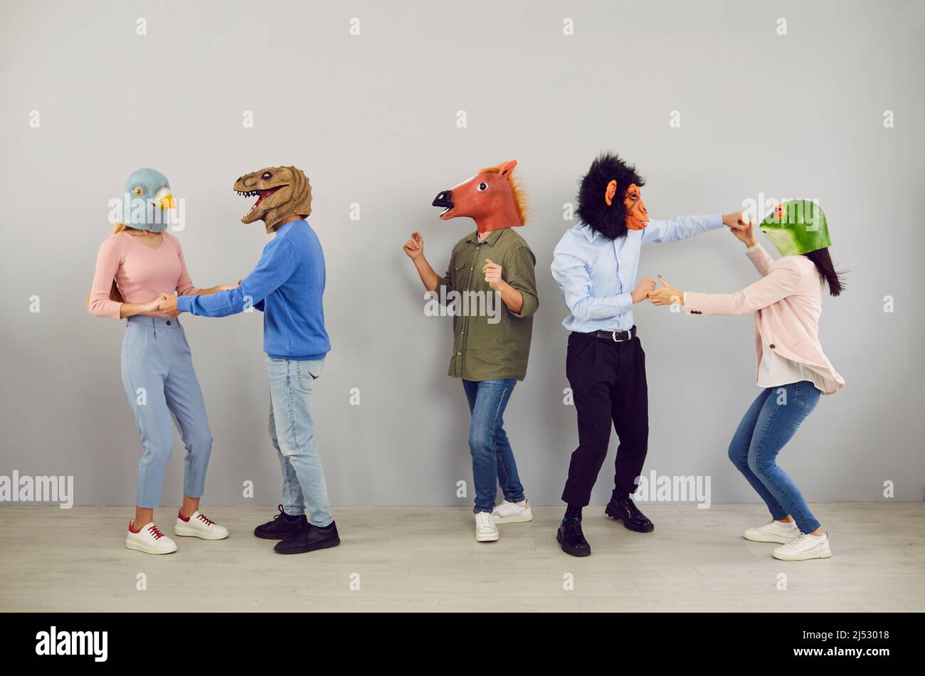 Fröhliche, exzentrische junge Menschen mit Köpfen verschiedener Tiere tanzen und haben gemeinsam Spaß. Stockfoto
