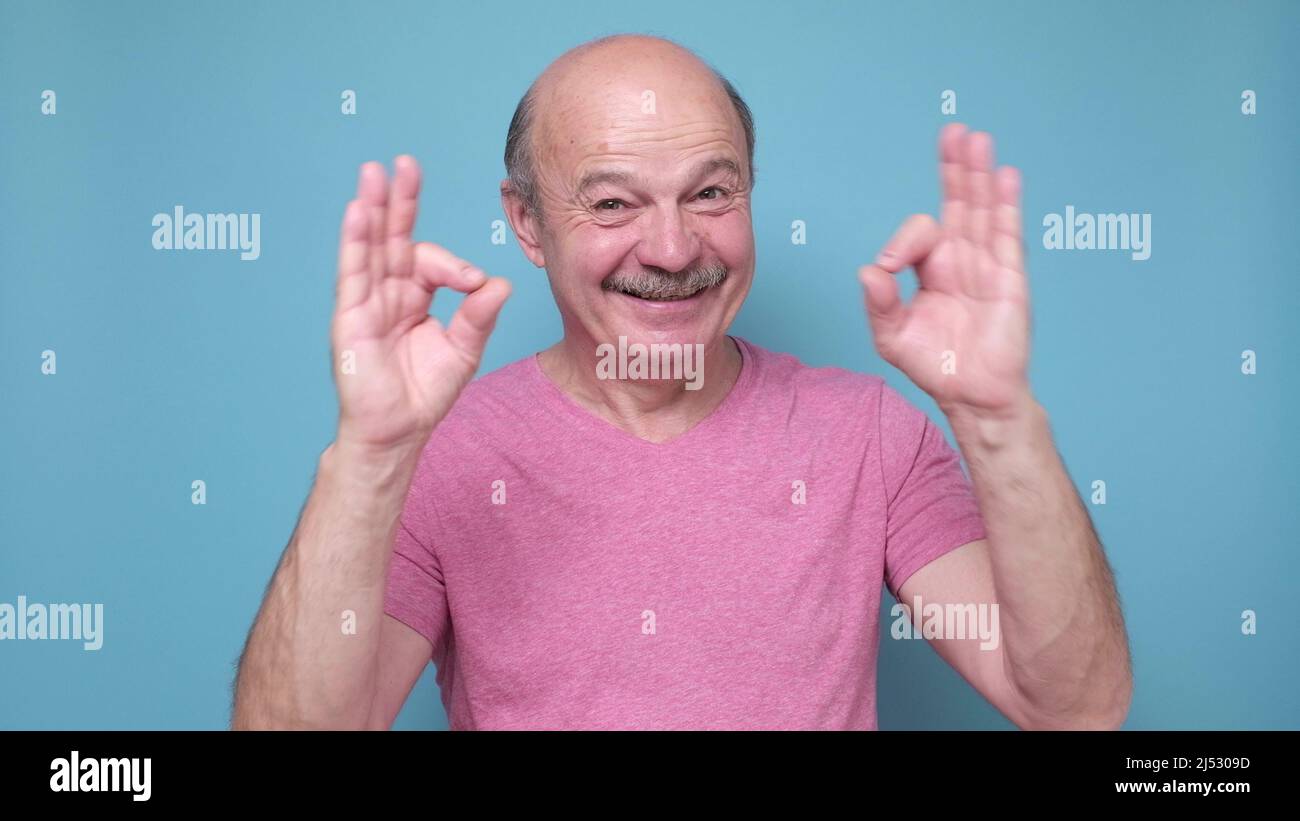 Ein Mann mittleren Alters lächelte positiv und tat es in Ordnung, ein Schild, das die Wahl genehmigte. Positive menschliche Emotionen im Gesicht. Stockfoto