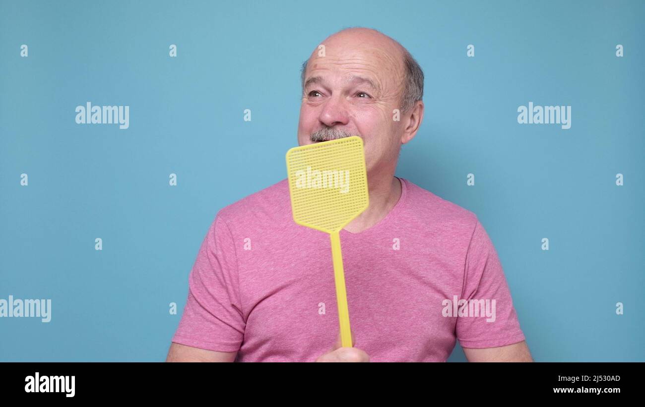 Hispanic Mann mit Fliegenklatsche versucht, Mücke auf blauem Hintergrund zu töten. Stockfoto