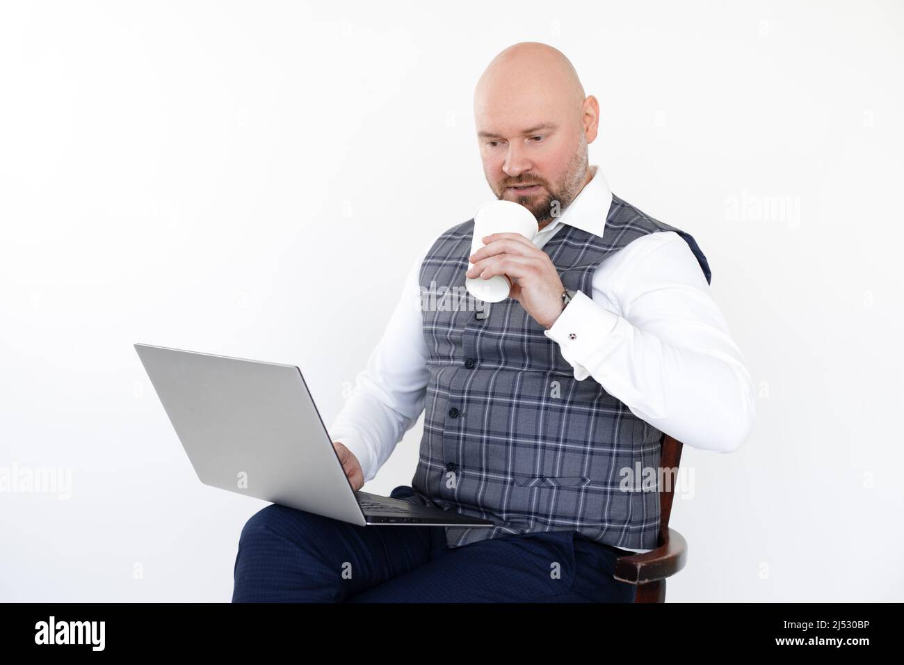 Porträt eines Geschäftsmannes in grauer Weste, blauer Jeans, weißem Hemd, Laptop in der Hand, weiße Tasse Kaffee zum Mitnehmen, Trinken. Stockfoto