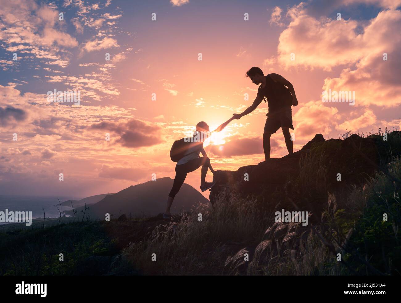 Wanderer arbeiten zusammen, um bei Sonnenaufgang einen Berg zu erklimmen. Helfende Hand. Stockfoto