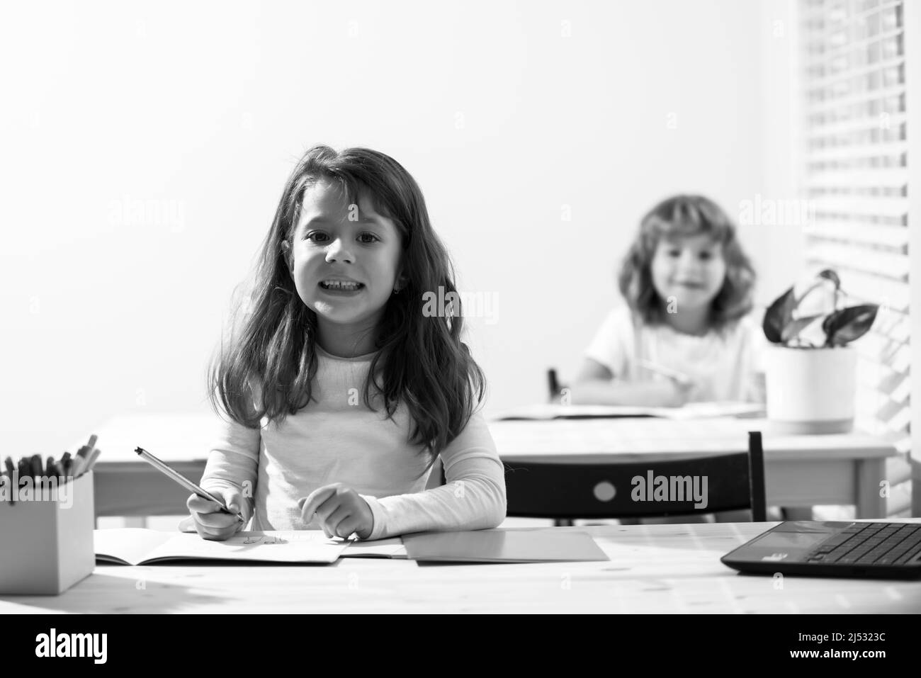 Lustige lächelnde Kinder im Klassenzimmer in der Schule. Schuljunge und Schulmädchen sitzen am Schreibtisch und schreiben einen Text. Stockfoto