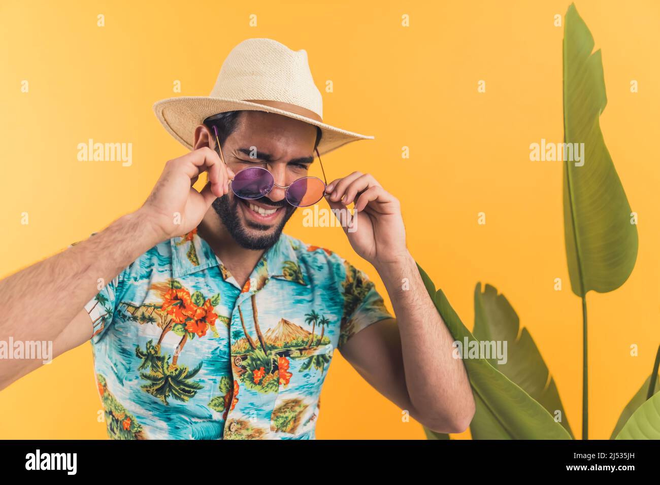 Schöner Latino-amerikanischer junger Mann in Sommerkleidung und mit Sonnenbrille, die auf orangefarbenem Hintergrund zwinkend ist, mit einem mittelgroßen Nahaufnahme-Studio, das im Sommer aufgenommen wurde. Hochwertige Fotos Stockfoto